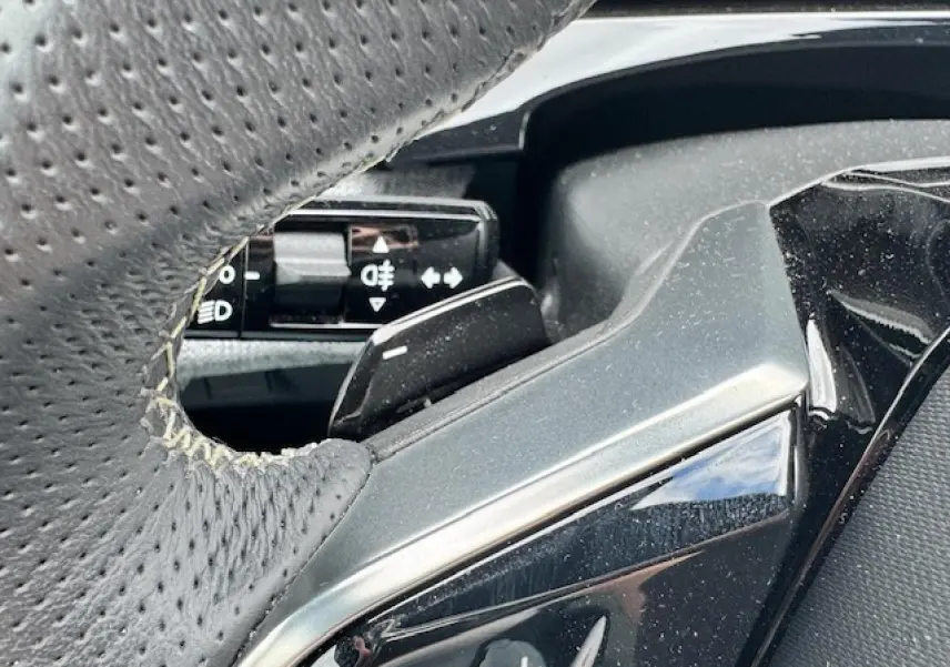 Détail du volant perforé gris avec commandes intégrées sur Peugeot 5008 gris titane 2024 hybride.