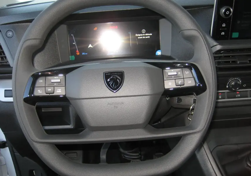 Volant noir avec logo Peugeot au centre, tableau de bord numérique et commandes intégrées dans un Peugeot Expert Fourgon blanc 2025.