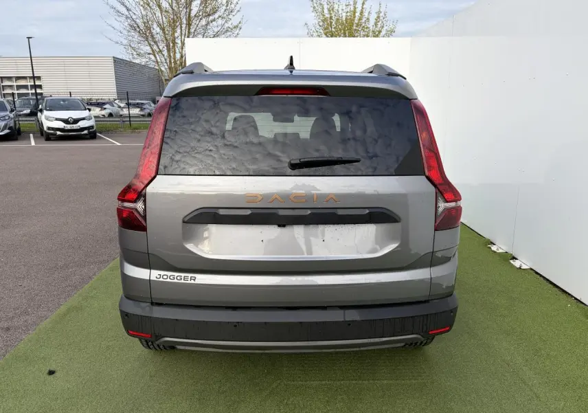 Vue arrière d'un Dacia Jogger gris schiste métal avec feux verticaux rouges et logo Dacia cuivré.