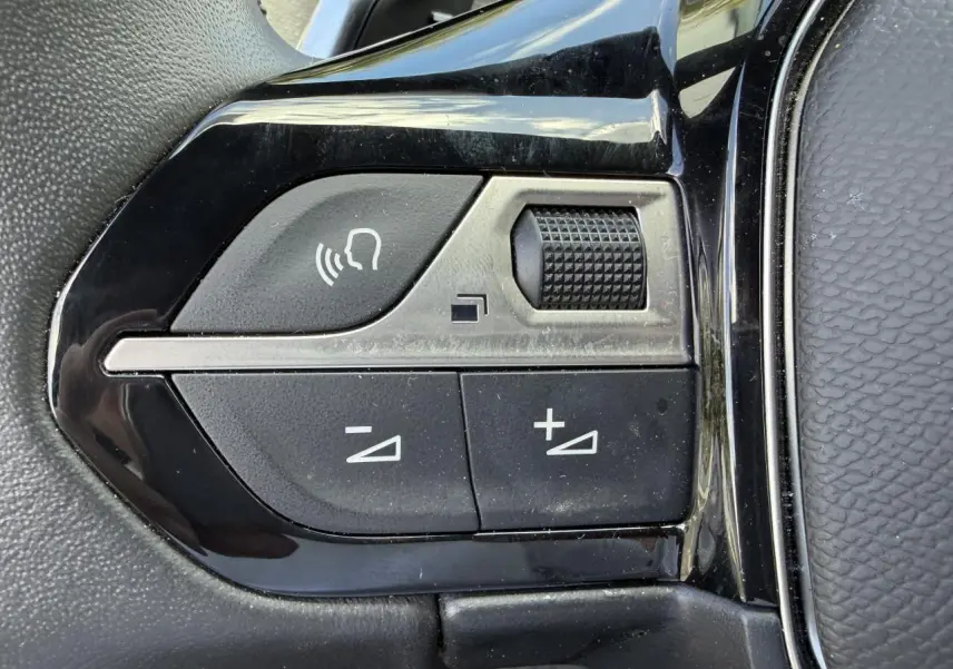 Gros plan sur les commandes de volume et de reconnaissance vocale sur le volant noir du Peugeot 3008 Plug-in Hybrid 2024.