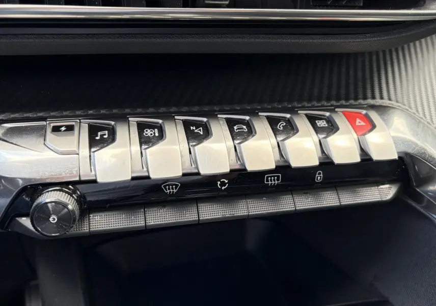 Gros plan sur la rangée de boutons métalliques du tableau de bord noir du Peugeot 3008 Plug-in Hybrid 2024.