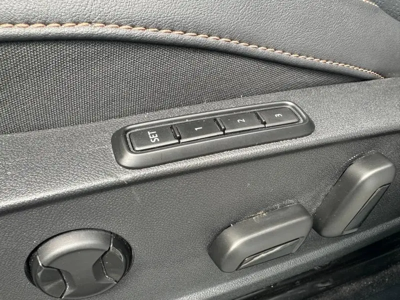 Gros plan sur les commandes de réglage électrique des sièges en tissu noir avec surpiqûres marron dans une CUPRA Formentor blanche.