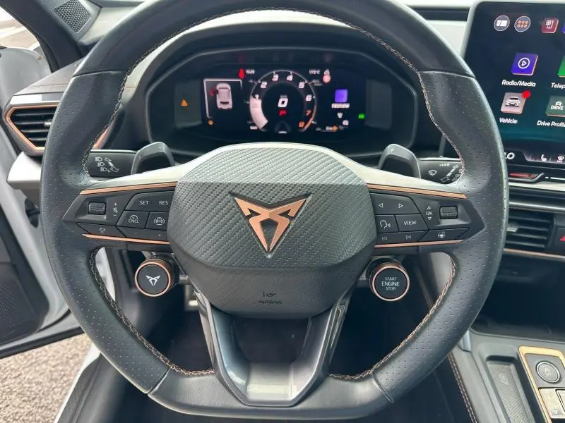 Vue rapprochée du volant cuir perforé noir avec logo CUPRA cuivré et commandes multifonctions, tableau de bord numérique visible.