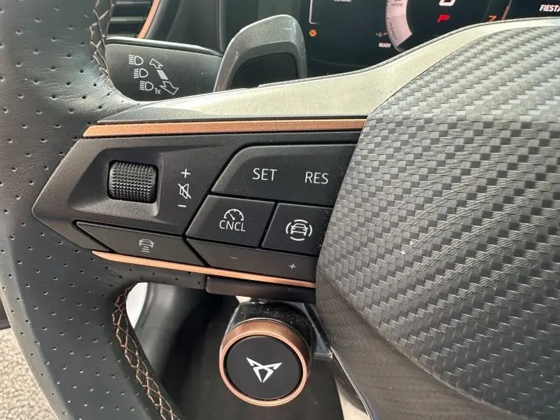 Gros plan sur les commandes à gauche du volant sport noir perforé avec surpiqûres cuivrées d'une CUPRA Formentor blanc Nevada.