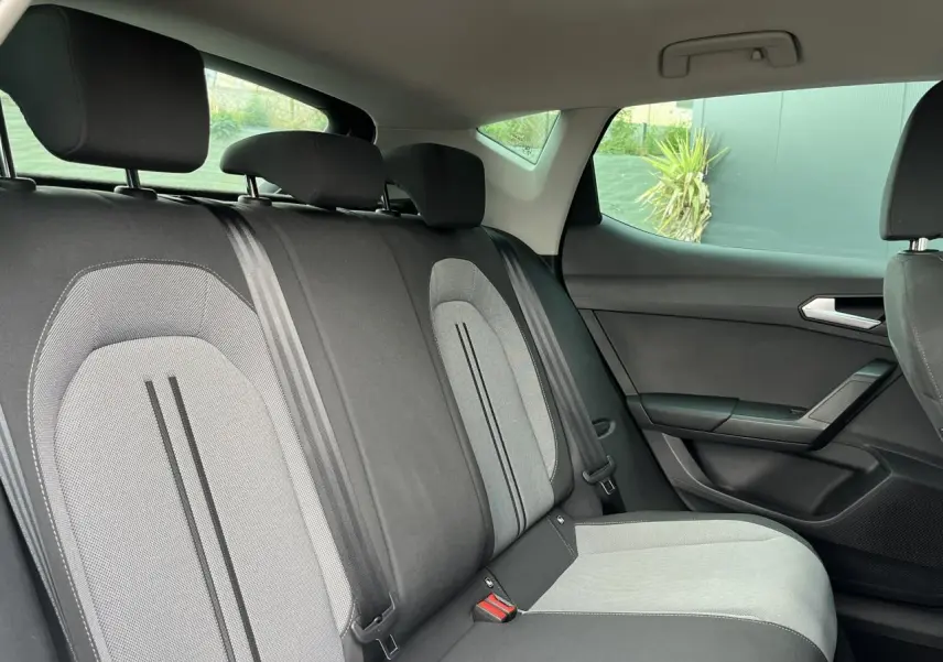 Vue côté droit de l'intérieur arrière de la SEAT LEON 2024 avec sièges tissu gris et ceintures noires.