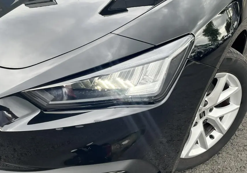 Gros plan sur le phare avant droit et la jante alliage blanche d'une SEAT LEON noire Minuit 2024.