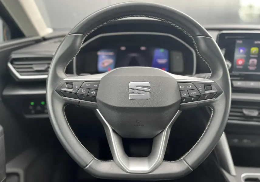 Volant cuir multifonction noir avec logo SEAT, cadrans numériques et écran tactile du tableau de bord en arrière-plan.