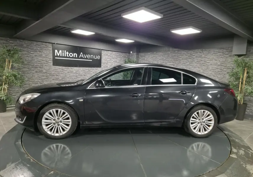 Profil côté gauche d'une berline Opel Insignia noire 2016 avec jantes alliage et vitres teintées en showroom.