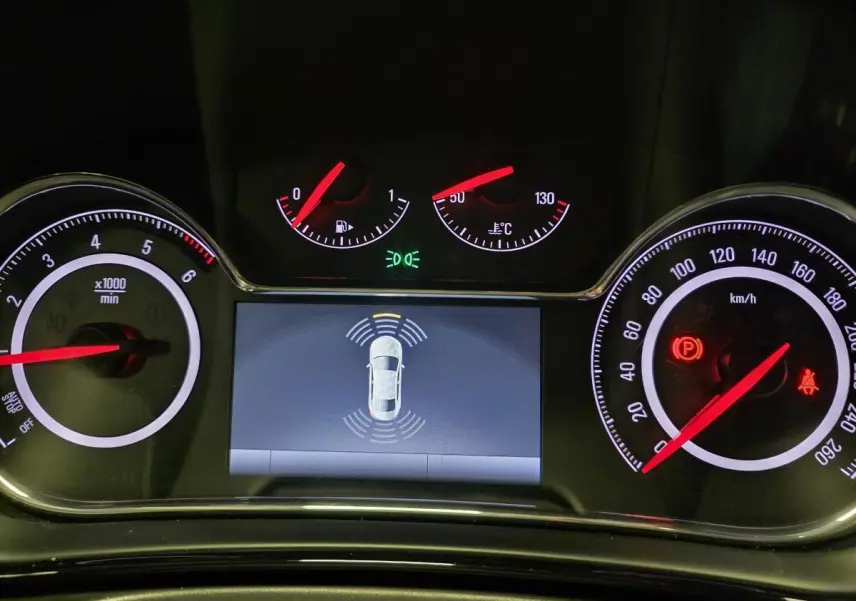 Tableau de bord noir de l'Opel Insignia 2016 avec affichage d'aide au stationnement et compteurs éclairés rouges.