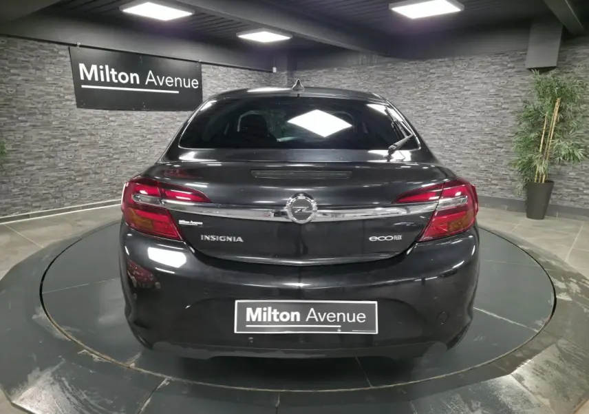 Vue arrière d'une Opel Insignia noire avec feux rouges et logo chromé dans un showroom intérieur.