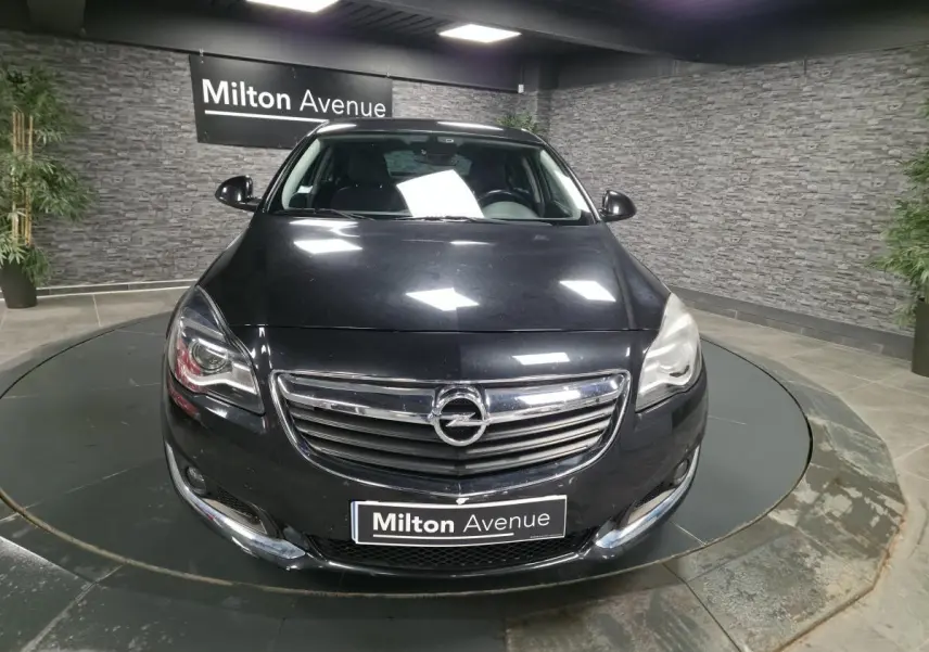 Vue frontale d'une Opel Insignia noire métallisée avec calandre chromée et phares allumés en showroom.