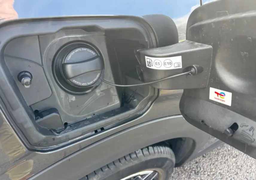 Vue rapprochée de la trappe à carburant côté gauche du Peugeot 3008 gris 2025 avec bouchon essence et jante alliage visible.