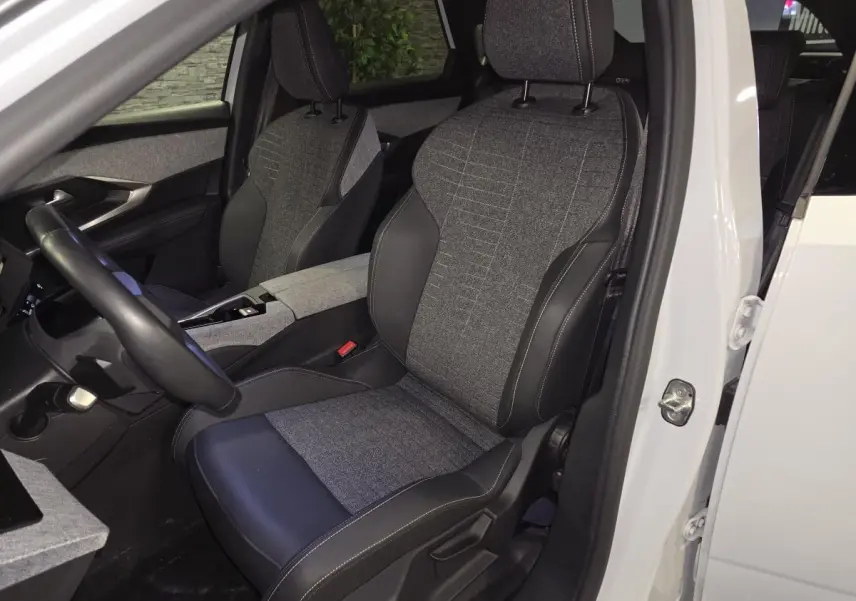 Vue intérieure côté conducteur du Peugeot 3008 blanc 2025, sièges tissu gris et cuir noir avec surpiqûres quartz.