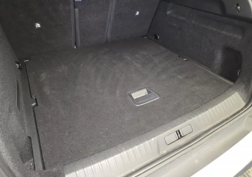Coffre spacieux et noir du Peugeot 3008 blanc 2025, vue intérieure depuis l'arrière avec plancher plat et poignées visibles.