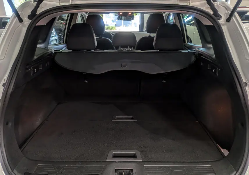 Vue arrière du coffre ouvert d'un Renault Kadjar blanc glacier 2020, montrant l'espace de chargement et la plage arrière noire.