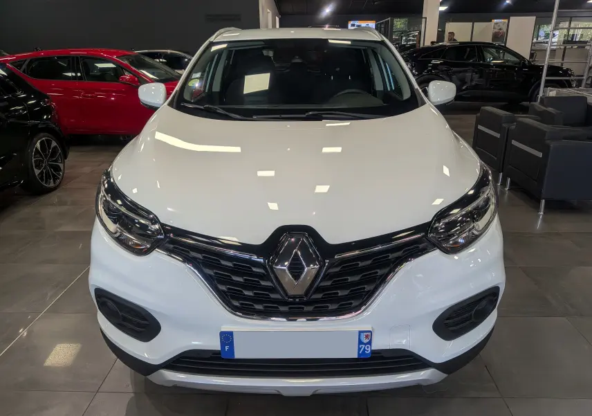 Vue avant d'un Renault Kadjar blanc Glacier 2020 en showroom, mettant en valeur la calandre noire et les phares modernes.