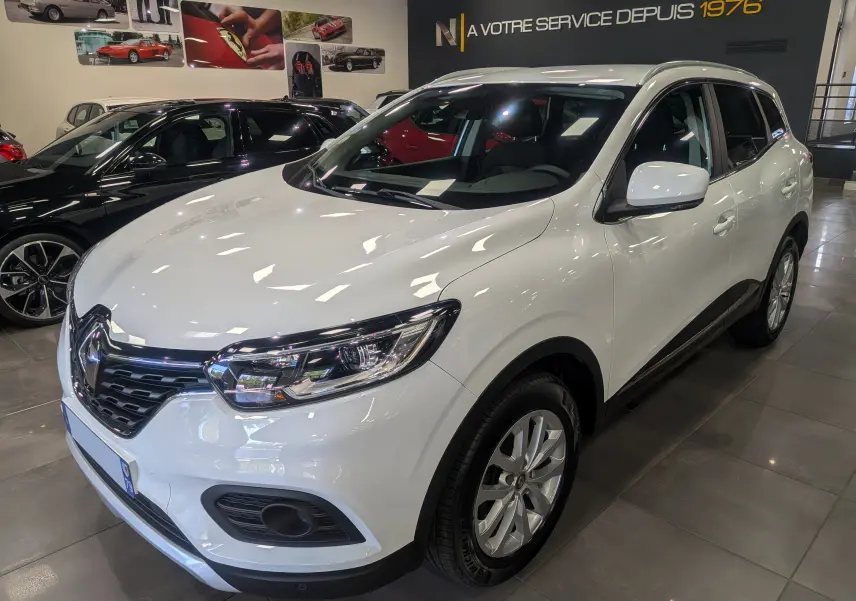 Renault Kadjar blanc Glacier en 3/4 avant droit dans un showroom avec éclairage intérieur et jantes alu.