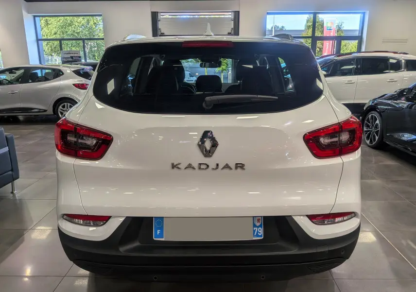 Vue arrière d'un Renault Kadjar blanc Glacier 2020 dans un showroom, avec feux arrière rouges et logo central visible.