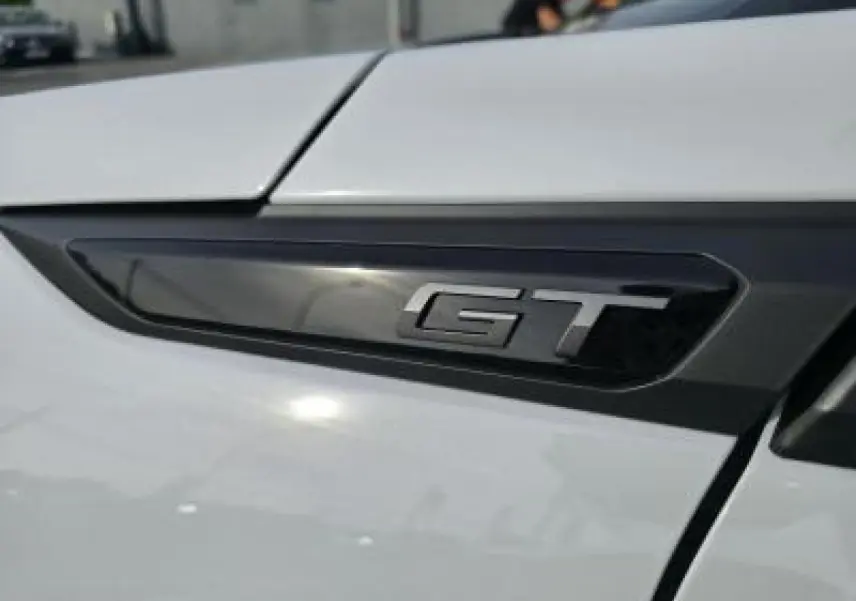 Gros plan sur l'emblème GT noir brillant sur la portière blanche du Peugeot 2008 II hybride 2025.