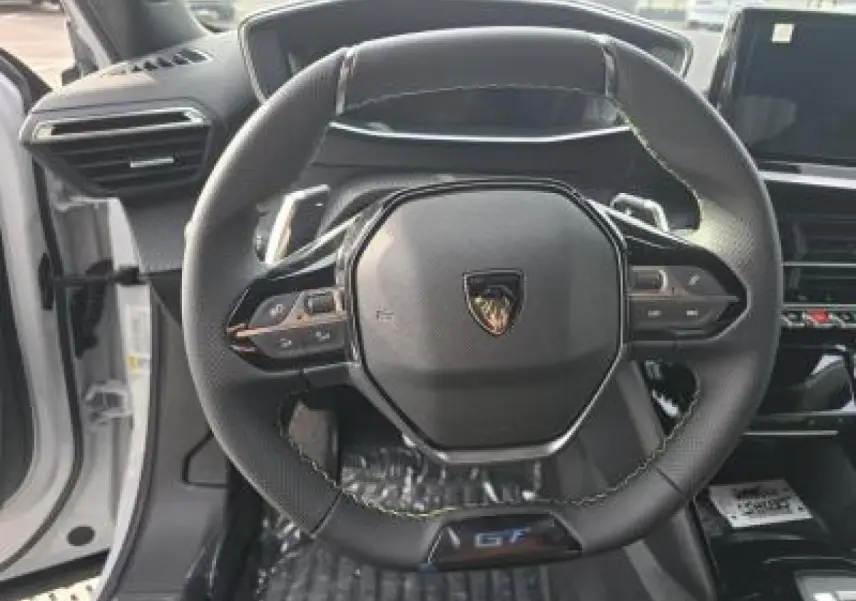 Gros plan sur le volant cuir noir avec logo Peugeot et badge GT du Peugeot 2008 hybride blanc, intérieur moderne.