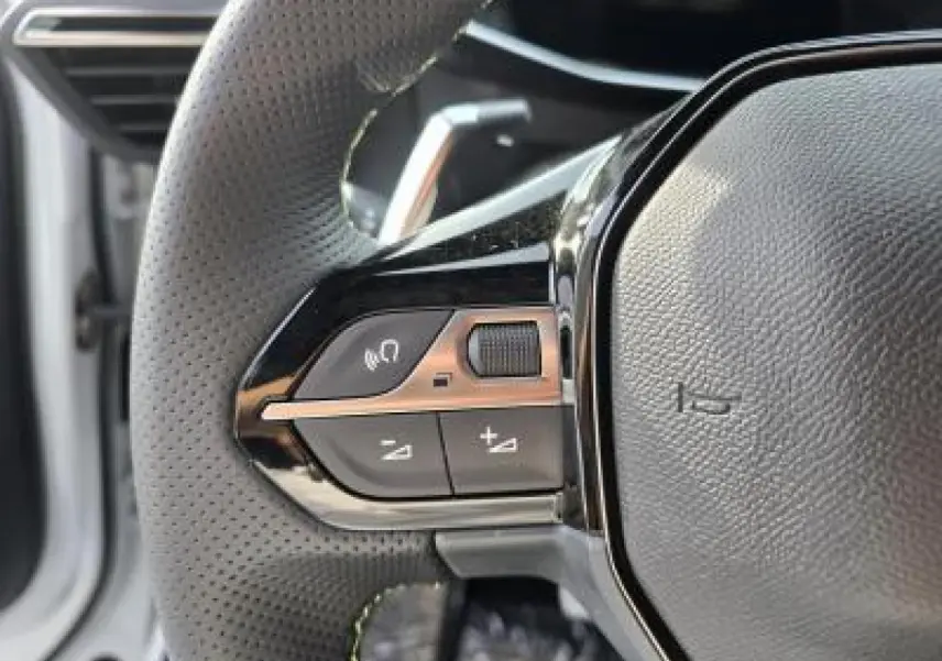 Gros plan sur les commandes gauche du volant cuir perforé de la Peugeot 2008 blanche toit noir, version hybride 2025.
