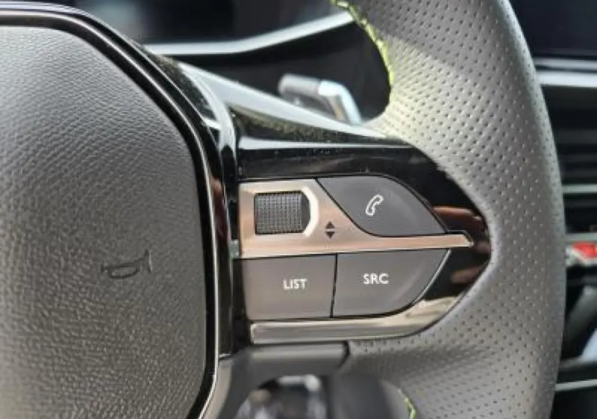 Gros plan sur les commandes gauche du volant cuir perforé du Peugeot 2008 blanc Okenite, version hybride 2025.