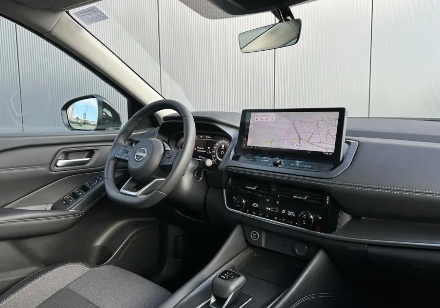Vue intérieure côté conducteur du Nissan Qashqai 2025 avec tableau de bord noir et écran tactile de navigation.