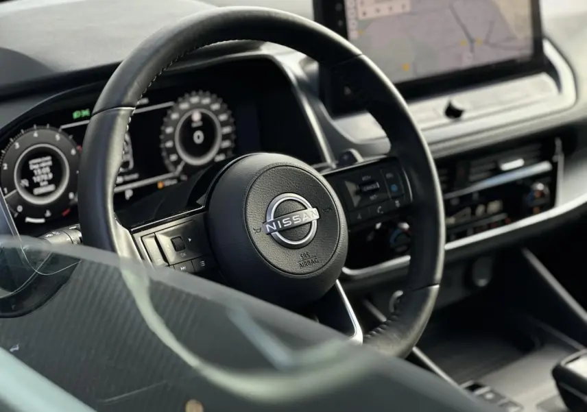 Gros plan sur le volant cuir noir du Nissan Qashqai 2025 avec tableau de bord numérique et écran tactile central.