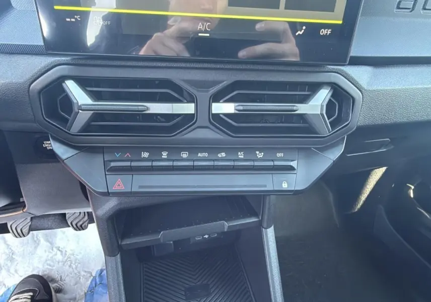 Détail du tableau de bord du Dacia Duster 2025 avec commandes climatisation et aérateurs hexagonaux noirs.