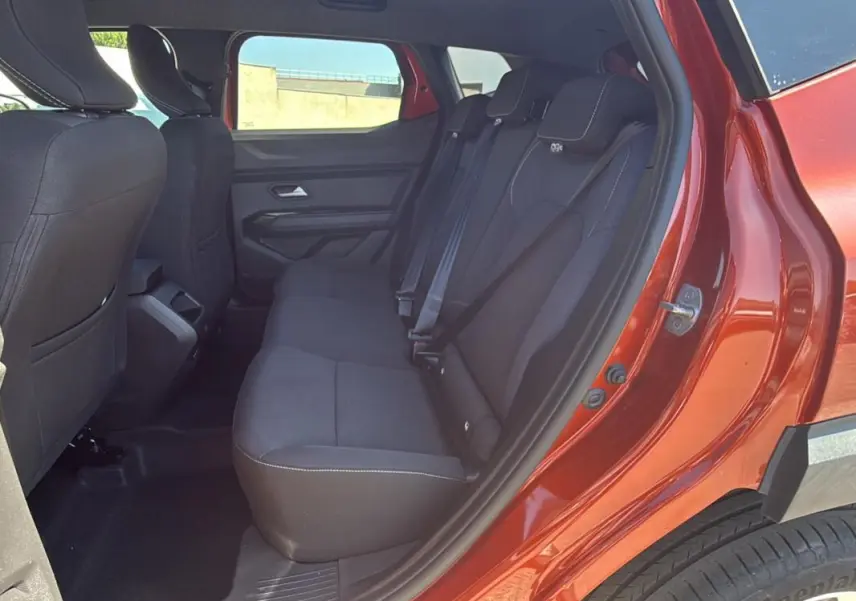 Vue intérieure des sièges arrière noirs du Dacia Duster orange 2025, porte arrière droite ouverte.