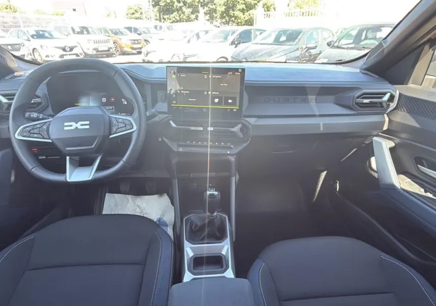 Vue intérieure avant du Dacia Duster 2025 avec tableau de bord moderne et écran tactile central.