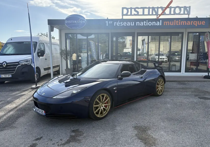 Lotus Evora 3.5 V6 S 2015 bleu Nightfall en 3/4 avant droit avec jantes dorées et aileron arrière visible.