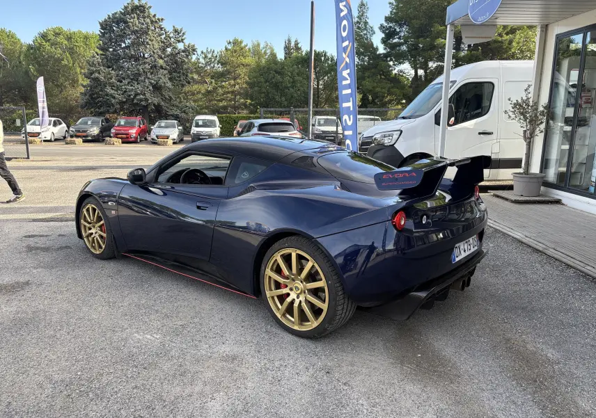 Lotus Evora 3.5 V6 S 2015 bleu Nightfall, vue 3/4 arrière droit avec aileron arrière et jantes dorées.