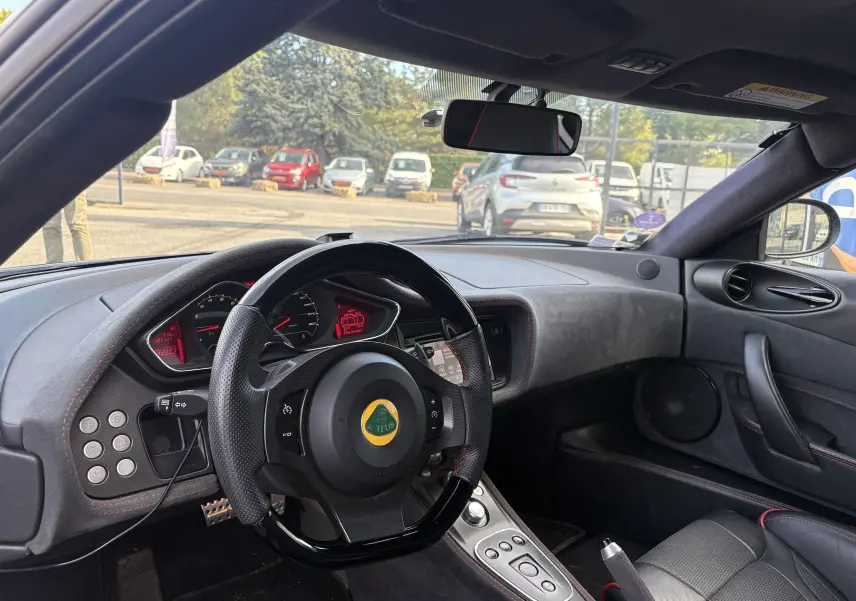 Intérieur du Lotus Evora 3.5 V6 S 2015 en Nightfall blue, vue du poste de conduite avec volant et tableau de bord visibles.