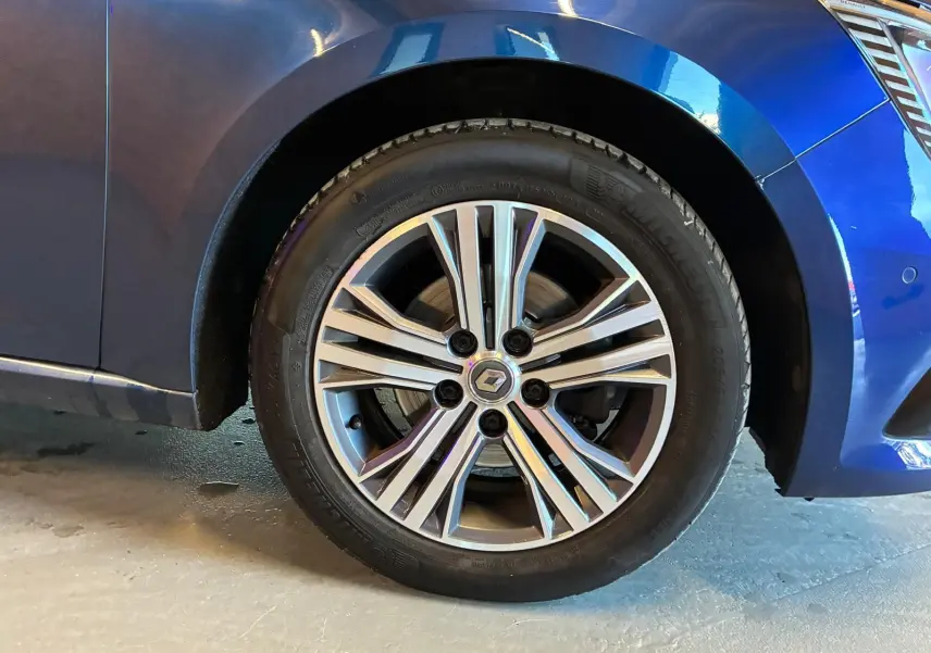 Gros plan sur la roue avant gauche d'une Renault Mégane bleu 2021 avec jante alliage bicolore et logo central Renault.