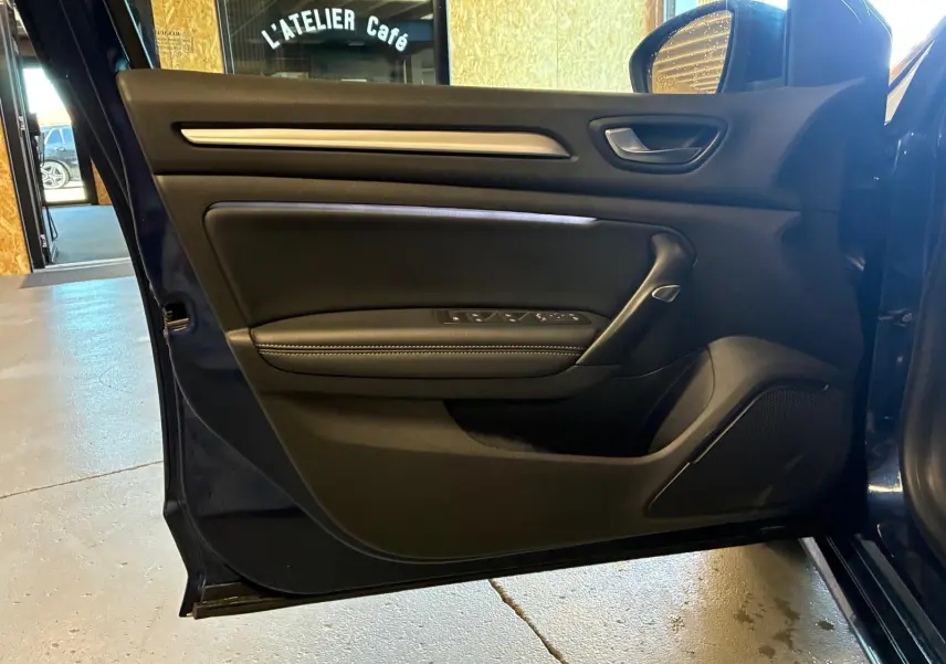 Vue rapprochée de la porte côté gauche ouverte d'une Renault Mégane bleu 2021, avec garniture intérieure noire et commandes électriques.