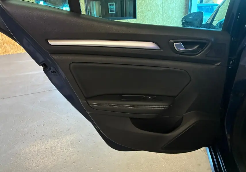 Vue rapprochée de la porte arrière gauche bleu foncé d'une Renault Mégane 1.5 DCI 115 Intens 2021 avec garniture noire et surpiqûres blanches.