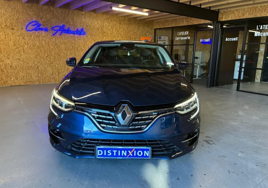 Vue frontale d'une Renault Mégane 1.5 dCi 115 Intens bleu, avec phares allumés dans un showroom moderne.
