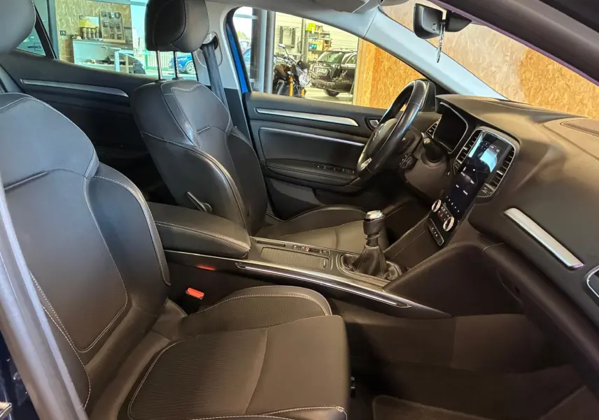 Intérieur avant de la Renault Mégane bleu 2021, sièges cuir noir, tableau de bord avec écran tactile et boîte manuelle.