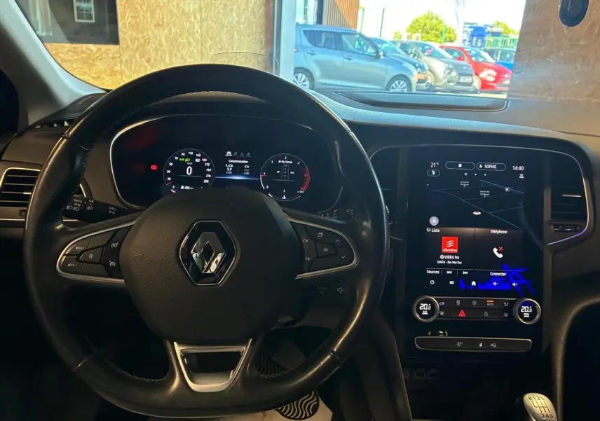 Vue intérieure centrée sur le volant noir Renault et l'écran tactile du tableau de bord de la Mégane bleue 2021.