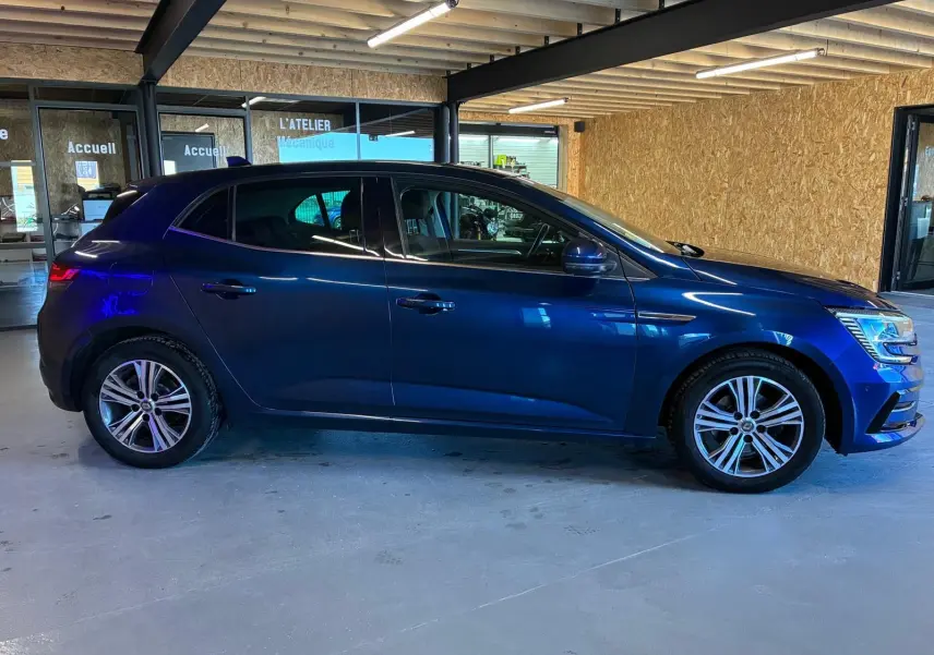 Profil droit d'une Renault Mégane 1.5 DCI 115 Intens bleu 2021 avec jantes alliage bicolores en intérieur d'atelier.