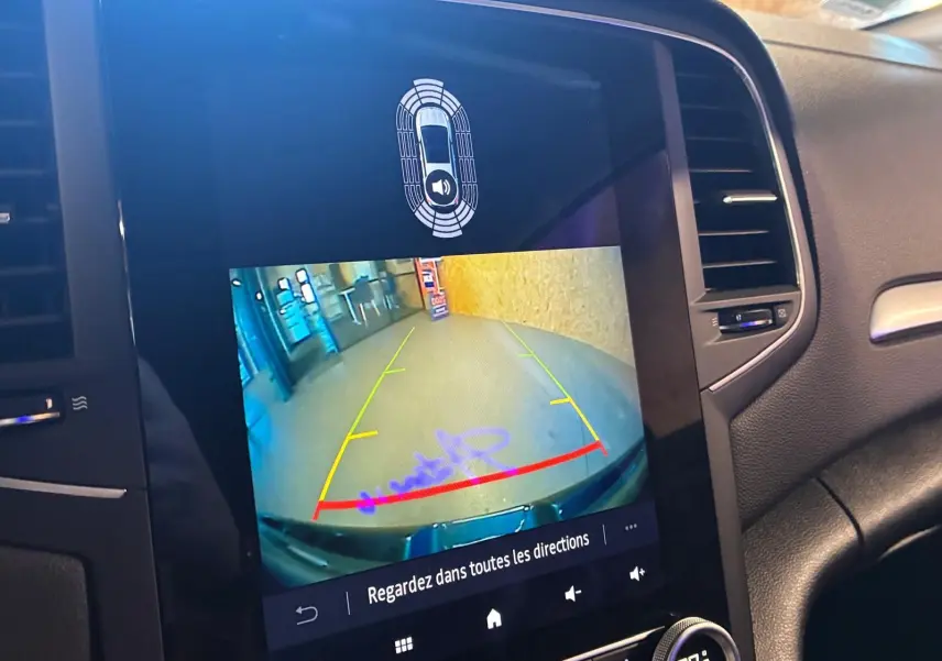 Vue rapprochée de l'écran multimédia d'une Renault Mégane bleu 2021 montrant la caméra de recul avec guidage coloré.