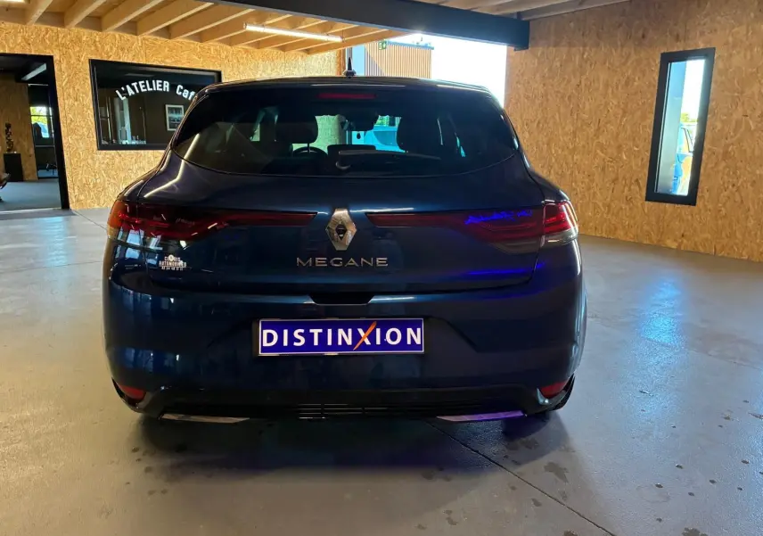 Vue arrière d'une Renault Mégane bleu foncé 2021 avec feux LED et logo Renault bien visibles dans un garage.