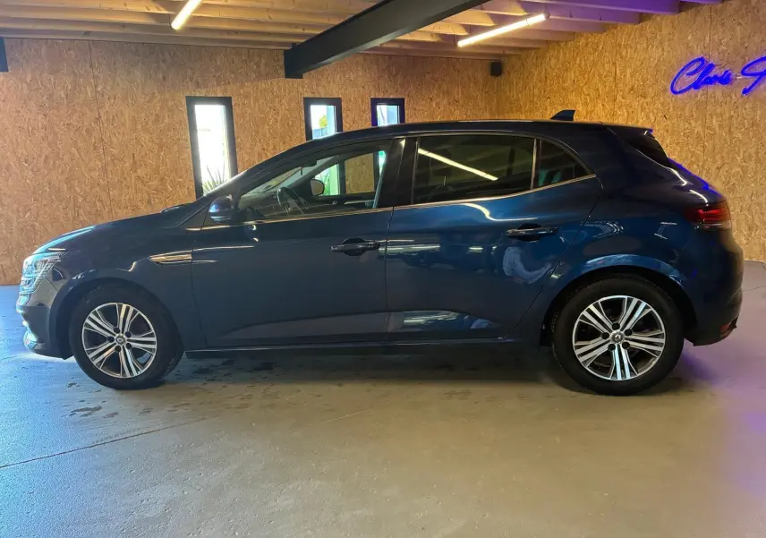 Profil côté gauche d'une Renault Mégane 1.5 dCi 115 Intens bleu, en intérieur avec jantes alliage bicolores visibles.