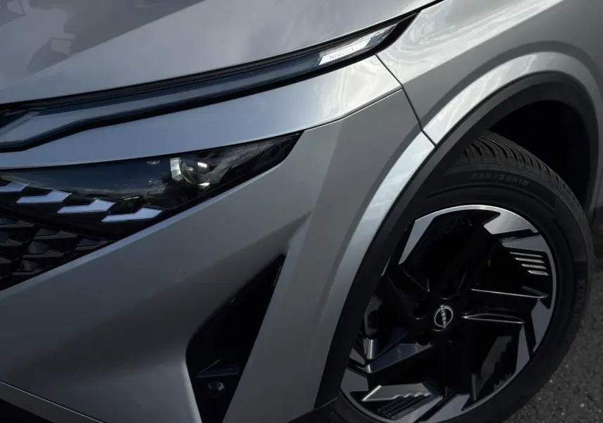 Gros plan sur l'avant droit gris argent du Nissan Qashqai 2025, mettant en valeur le phare LED et la jante alliage noire.