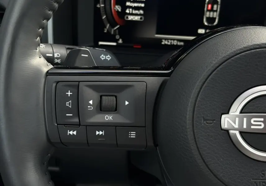 Gros plan sur les commandes au volant gauche du Nissan Qashqai gris argent 2025 avec affichage numérique en arrière-plan.