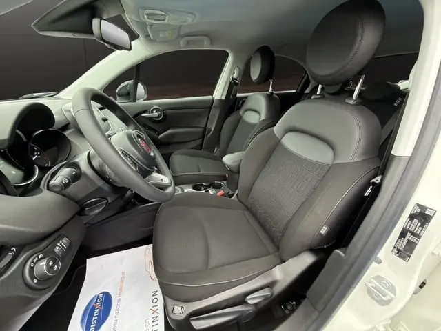 Vue intérieure côté conducteur de la FIAT 500X blanche 2023, sièges noirs avec volant multifonctions en alu et cuir synthétique.