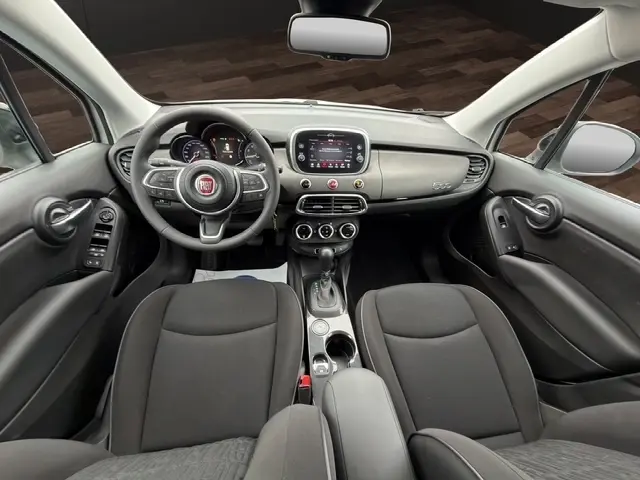 Vue intérieure avant de la Fiat 500X 2023, tableau de bord noir avec volant multifonctions en alu et cuir synthétique.