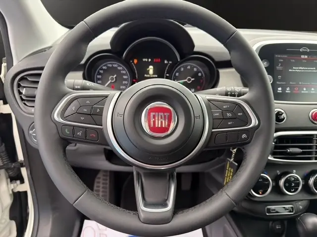 Vue rapprochée du volant multifonctions en cuir noir avec logo FIAT rouge au centre, tableau de bord et écran tactile visibles.