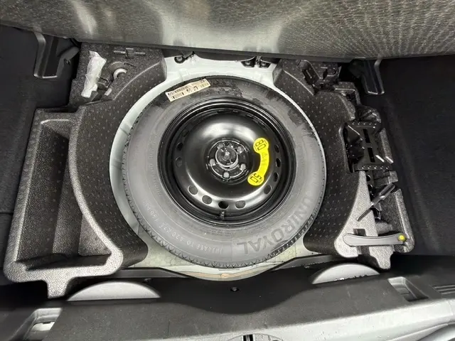 Vue du coffre ouvert d'une Fiat 500X blanche 2023, montrant la roue de secours compacte et son rangement en mousse noire.
